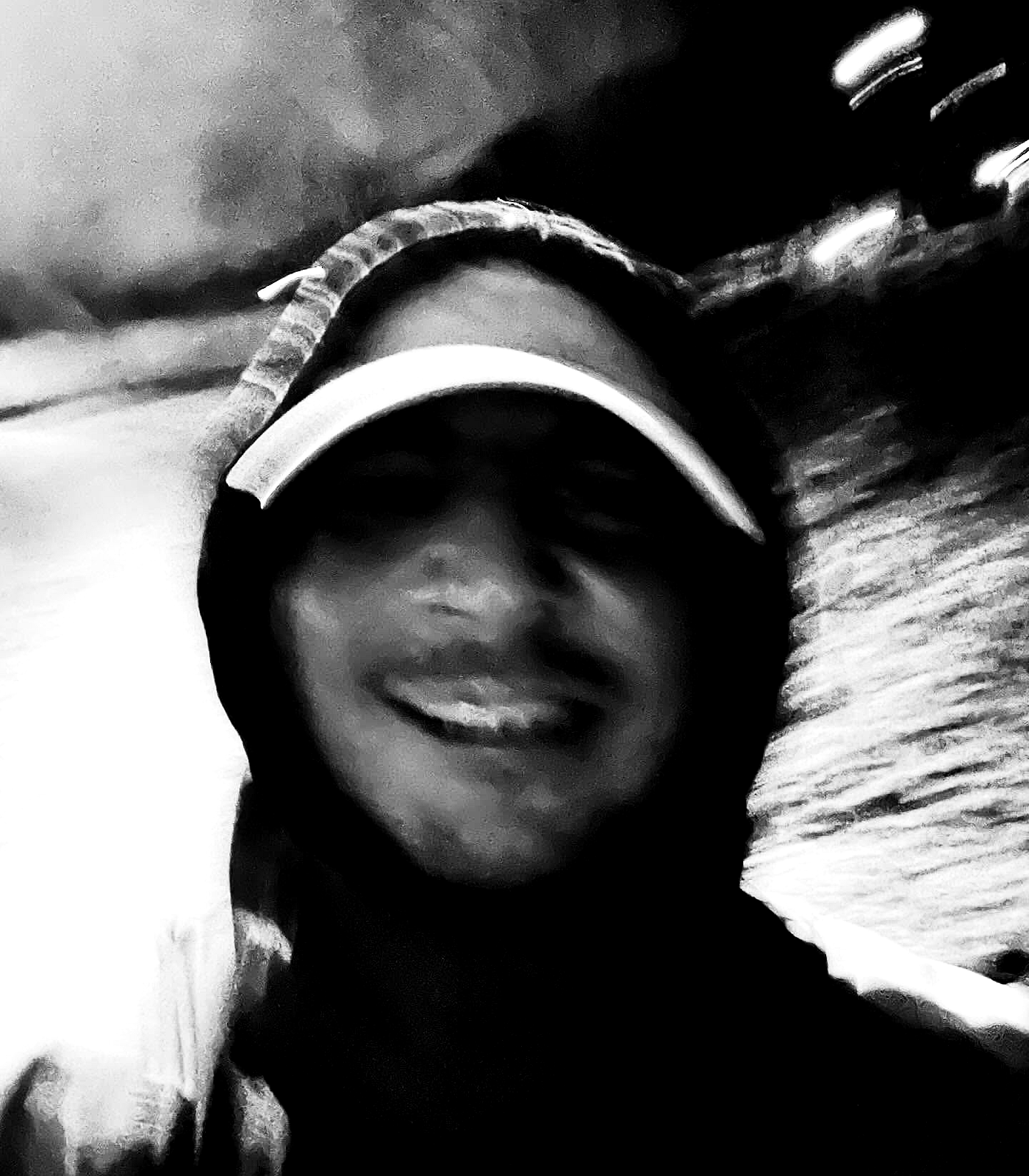 A blurred close selfie in motion, with a visor and grin dissolved into high-contrast black-and-white grain.